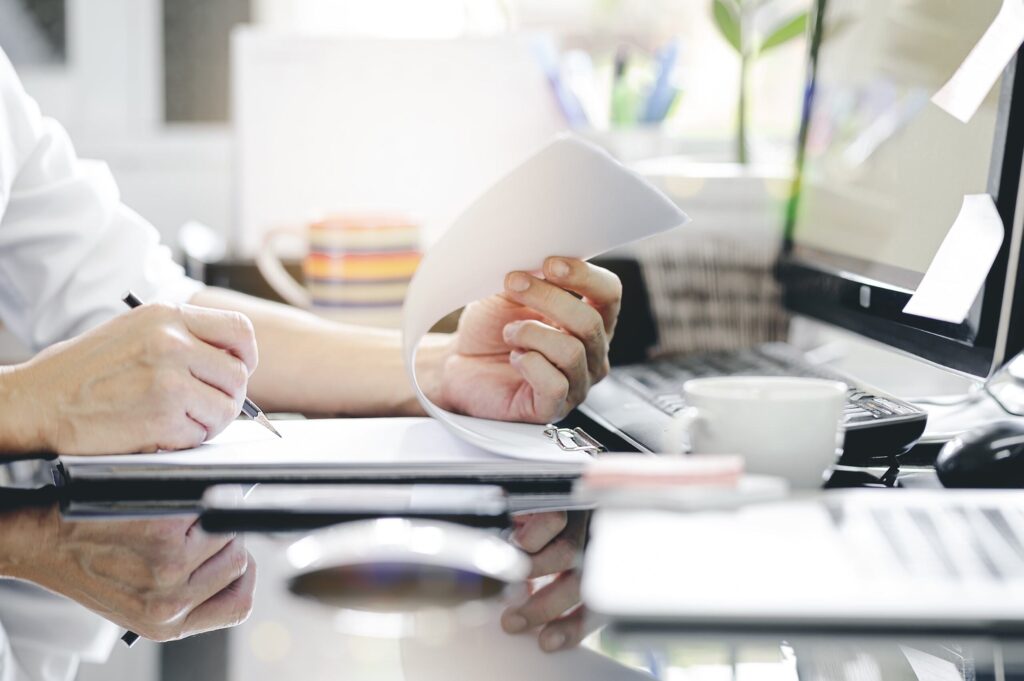 man hand using pencil writing clipboard while sitting office desk working with computer