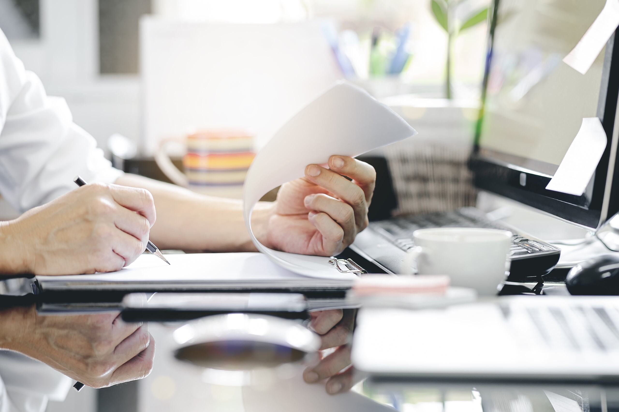man hand using pencil writing clipboard while sitting office desk working with computer