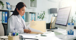 Computer, woman and doctor with paperwork in clinic for research report, diagnosis or treatment. Tech, medical service and female healthcare worker with referral document for notes in hospital office.