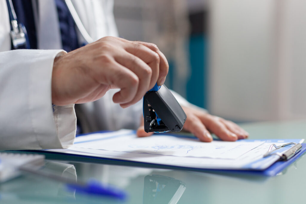 Hand of physician using medical seal on prescription paper in cabinet